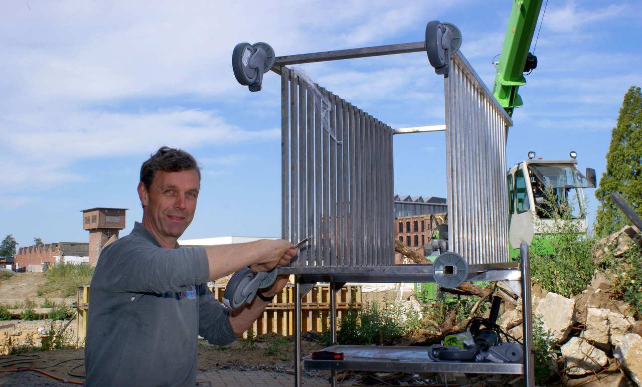 Norbert Nienhaus montiert neue Räder an einen Kühlwagen. Im Hintergrund sieht man Bauarbeiten.