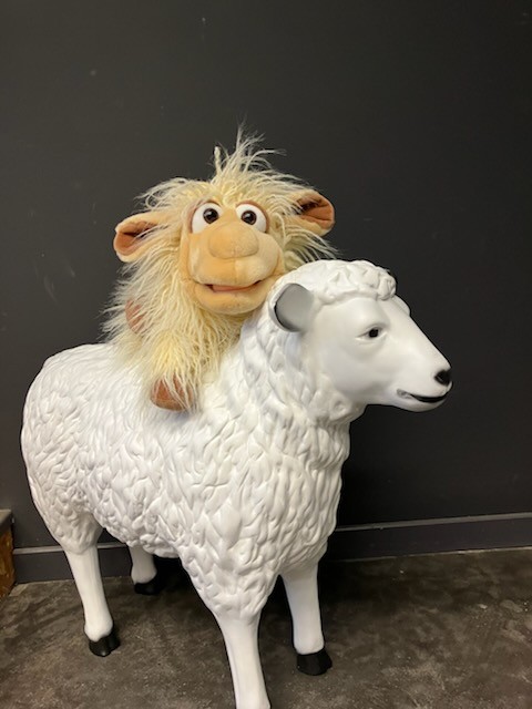 Eine Schaf-Handpuppe sitzt auf einer Schaf-Figur