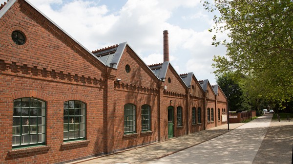 Blick auf die Fassade der Weberei mit dem dahinterliegenden Fabrikschornstein