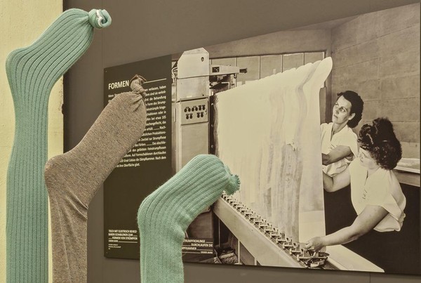Blick in die Ausstellung mit verschiedenen Socken und großformatiger schwarz weiß Aufnahme im Hintergrund.