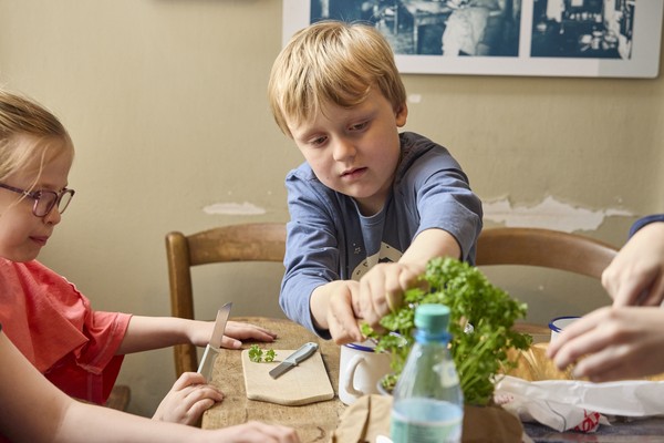 Kinder sitzen am Tisch auf dem Brot, Butter und Kräuter stehen.