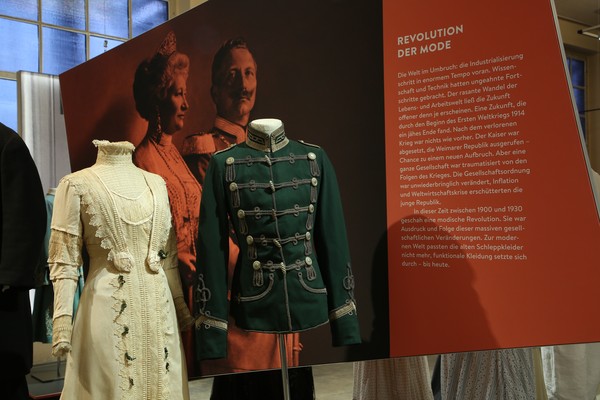 Blick in die Ausstellung: Weißes Kleid und Wrack vor der Ausstellungstafel "Revolution der Mode".