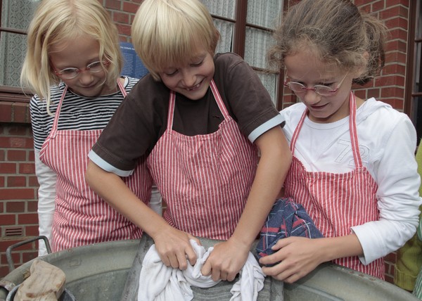 Drei Kinder waschen Kleidung am Waschbrett.
