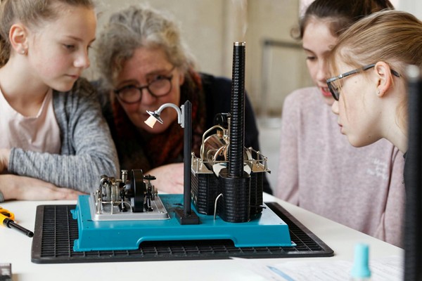 Kinder schauen sich gemeinsam mit einer Museumspädagogin ein Modell an.