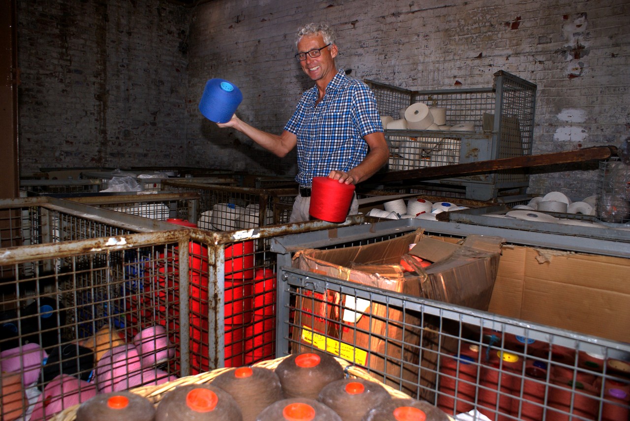 Museumsleiter Dr. Hermann Josef Stenkamp hat zwei farbige Garnrollen in der Hand. Um ihn herum stehen Gitterboxen mit vielen weiteren Garnrollen.