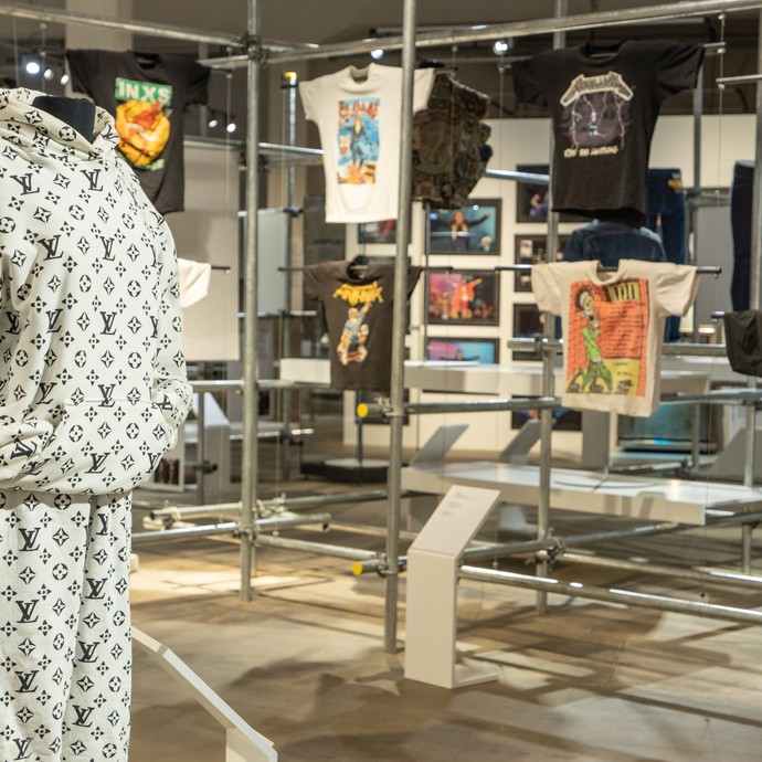 Blick in die Ausstellung: Im Vordergrund ein moderner Jogginganzug, im Hintergrund diverse T-Shirts. (vergrößerte Bildansicht wird geöffnet)