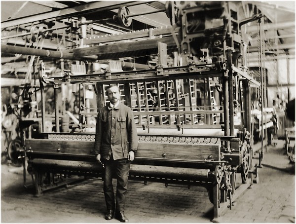 Historische Schwarzweiß-Aufnahme eines Arbeiters, der vor einer Maschine steht