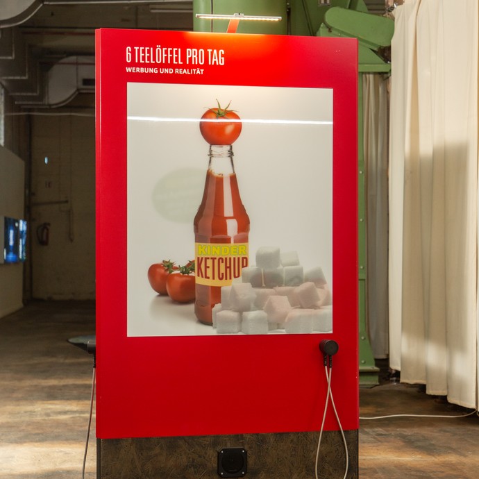 Blick in die Ausstellung: Großes Plakat mit  Ketchupflasche inklusive Hörstation (vergrößerte Bildansicht wird geöffnet)