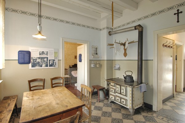 Blick in die Küche des Arbeiterhauses mit Ofen und Eßtisch.